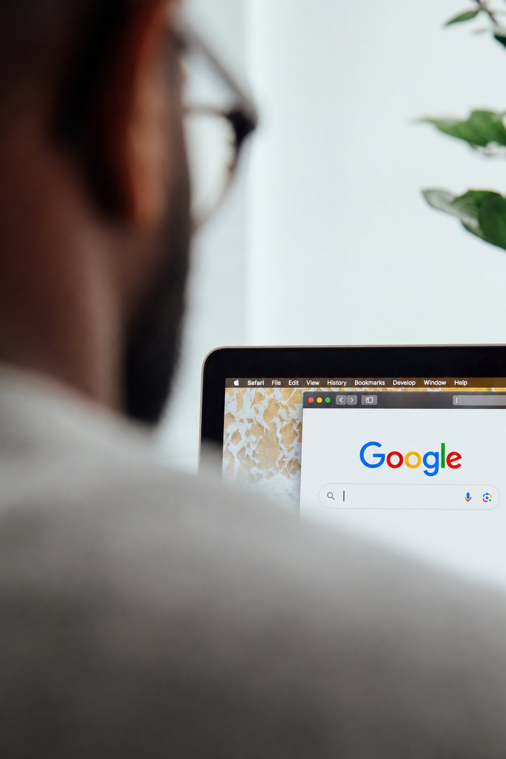 A person with glasses looking at the Google search homepage on a laptop screen